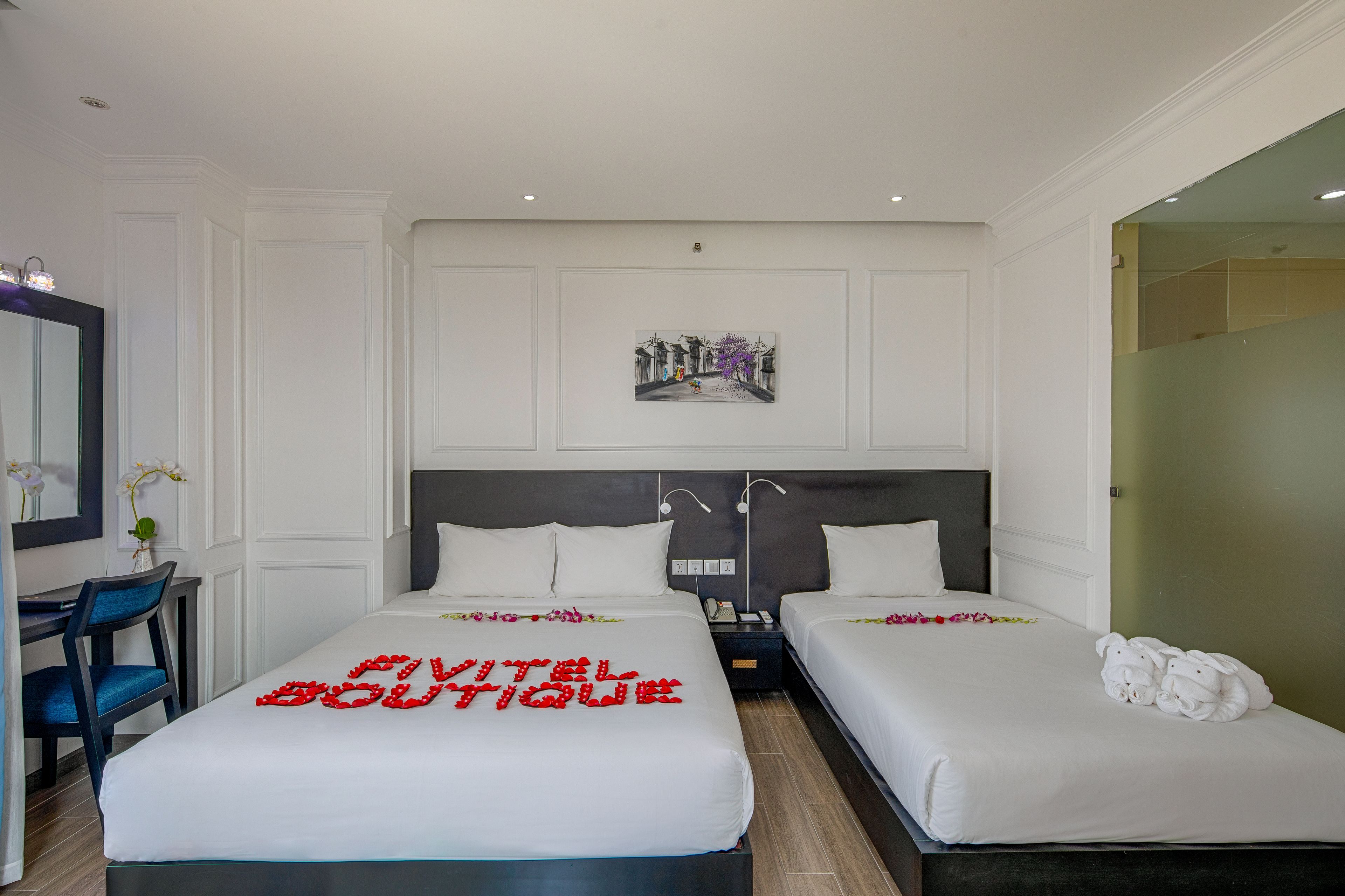 A hotel room with two beds, a desk, and a mirror.