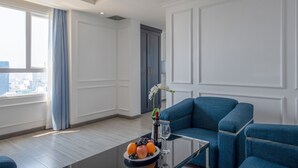 Una sala de estar moderna con una mesa de centro de vidrio, sofás azules, un florero con flores y vistas a la ciudad a través de amplios ventanales.