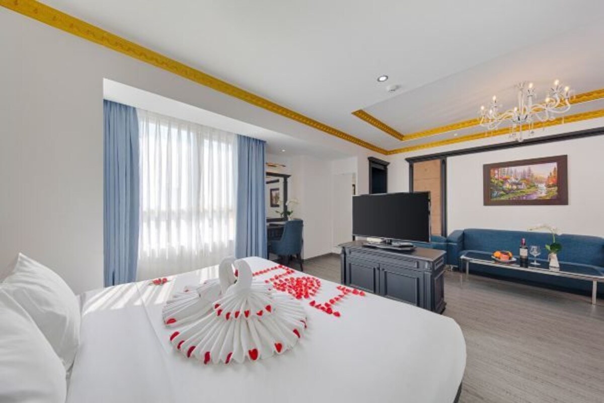 A hotel room with a large bed, a TV, a sofa, and a chandelier.