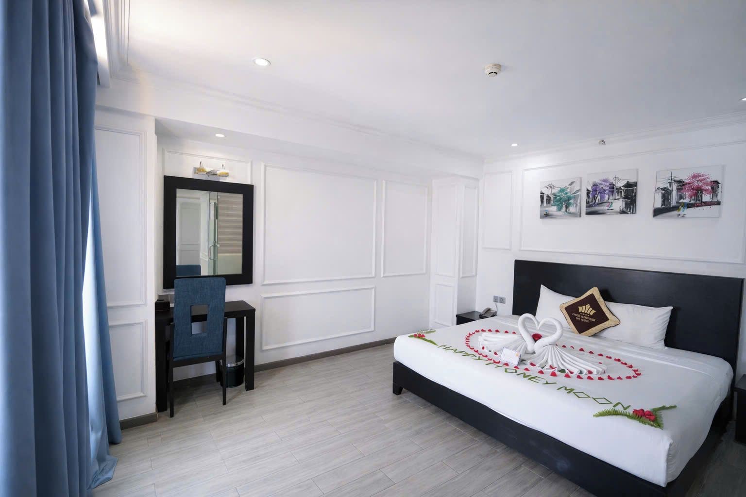 A hotel room with a bed, a desk, a chair, a mirror, and a wall with pictures.