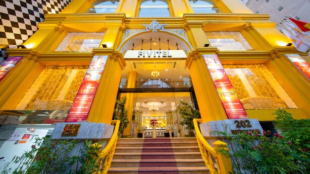 Una entrada de hotel con fachada a cuadros, un llamativo letrero 'FIVITEL' y una escalera que conduce al vestíbulo.