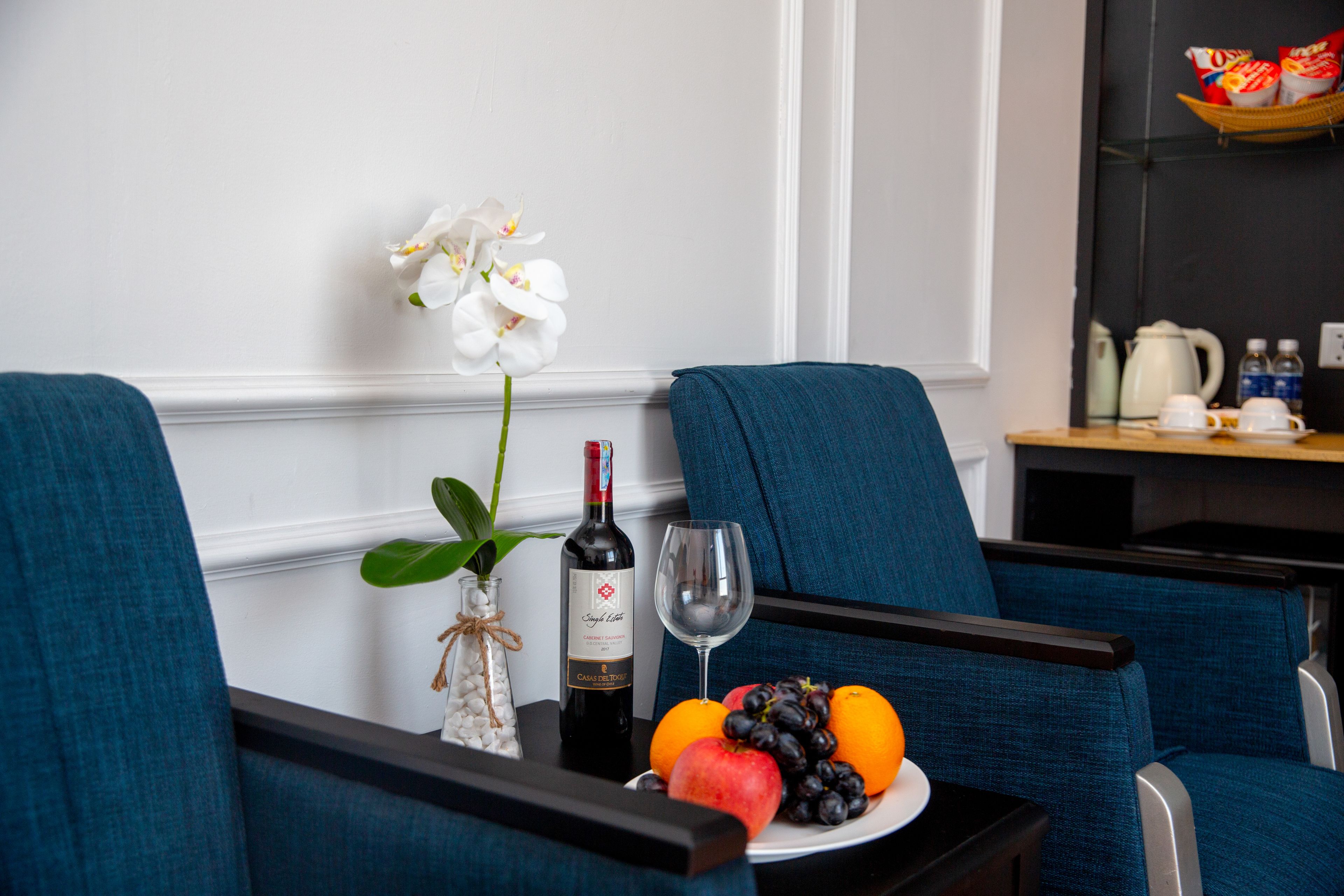 Un comedor con una mesa dispuesta para dos personas, que incluye una botella de vino, una copa y un plato de fruta.