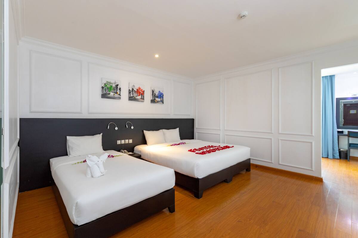 Habitación de hotel con dos camas, piso de madera y vista al pasillo.