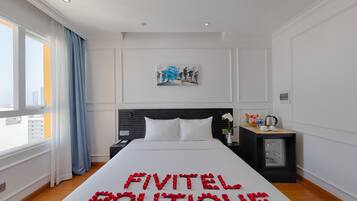 A hotel room with a bed, a nightstand, a window with curtains, and a wall-mounted artwork.