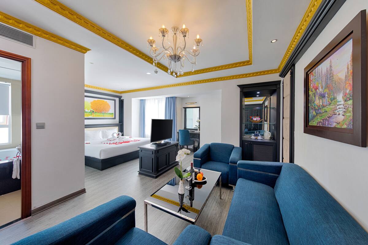 Habitación de hotel con cama, televisor, sofá, mesita de centro y un cuadro en la pared.