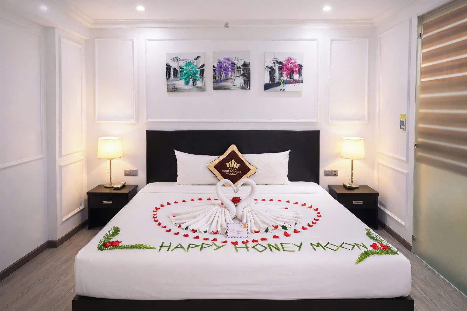 Habitación de hotel con una cama hecha con cuidado, una decoración central con forma de cisne y un mensaje que dice 'Luna de Miel Feliz'.