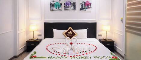 Habitación de hotel con una cama hecha con cuidado, una decoración central con forma de cisne y un mensaje que dice 'Luna de Miel Feliz'.