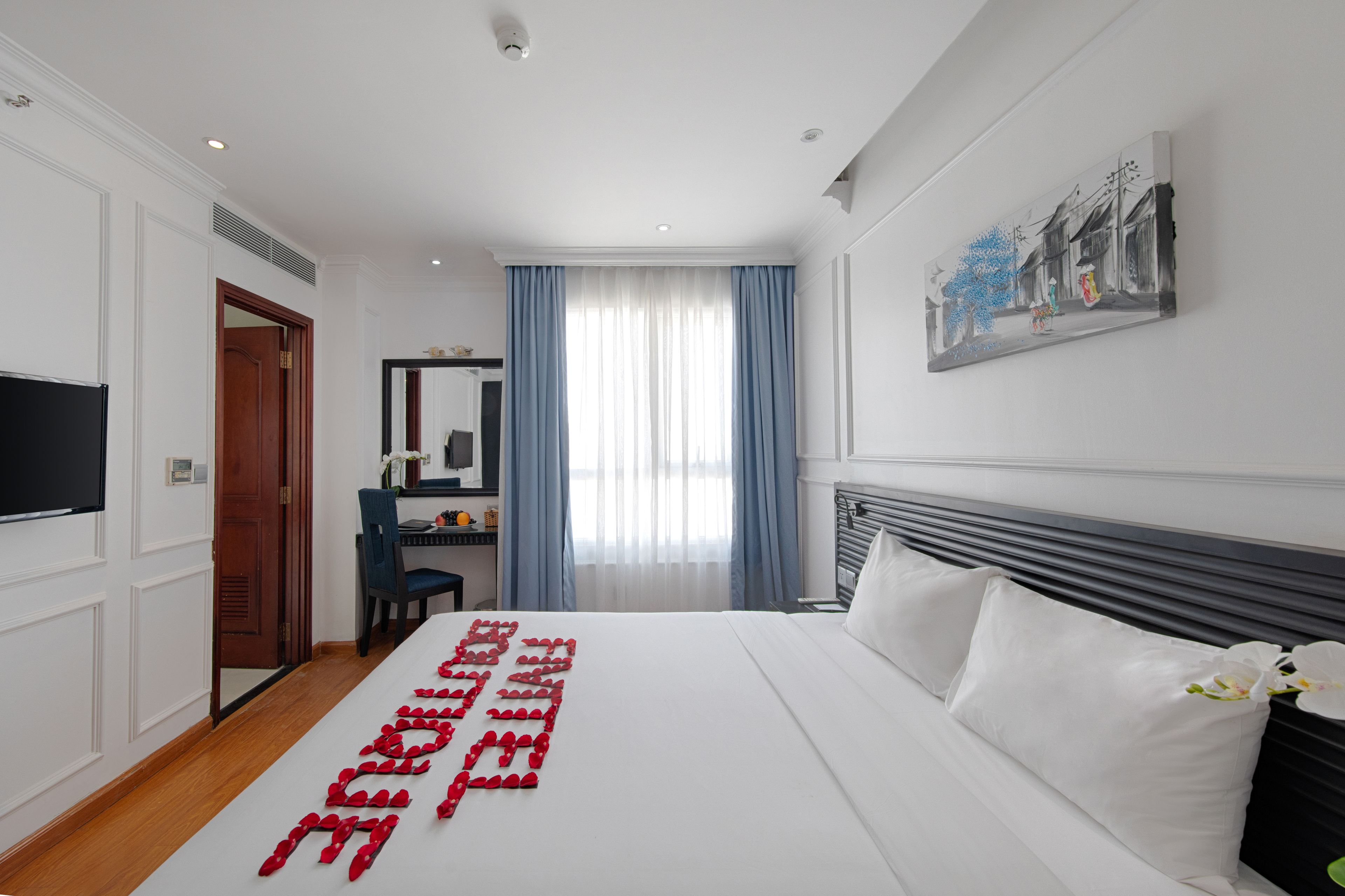 Una habitación de hotel con una cama grande, un escritorio, una silla, un televisor y un cuadro en la pared.