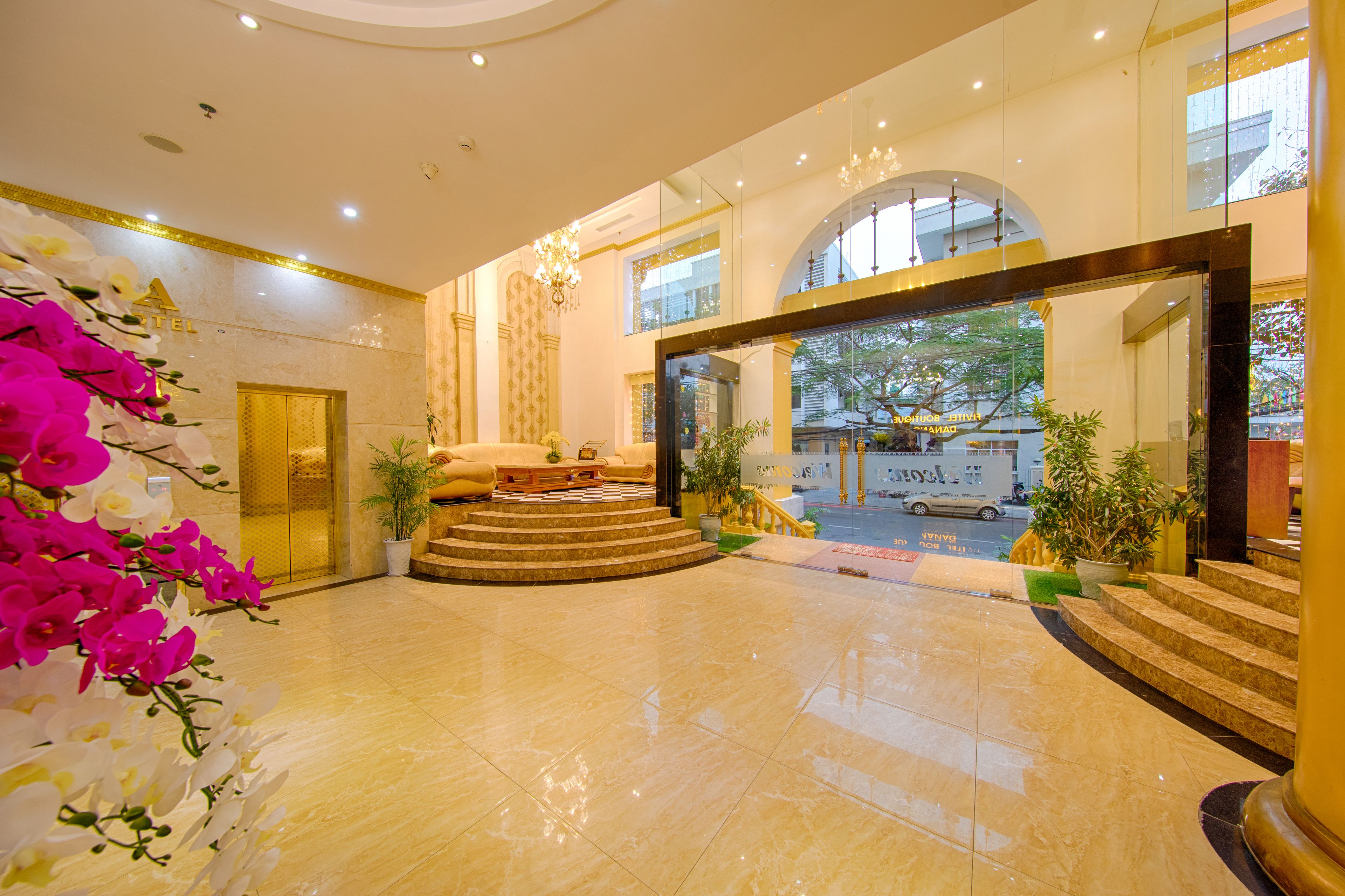 A hotel lobby with a marble floor, a reception desk, a staircase, and a view of the street outside.