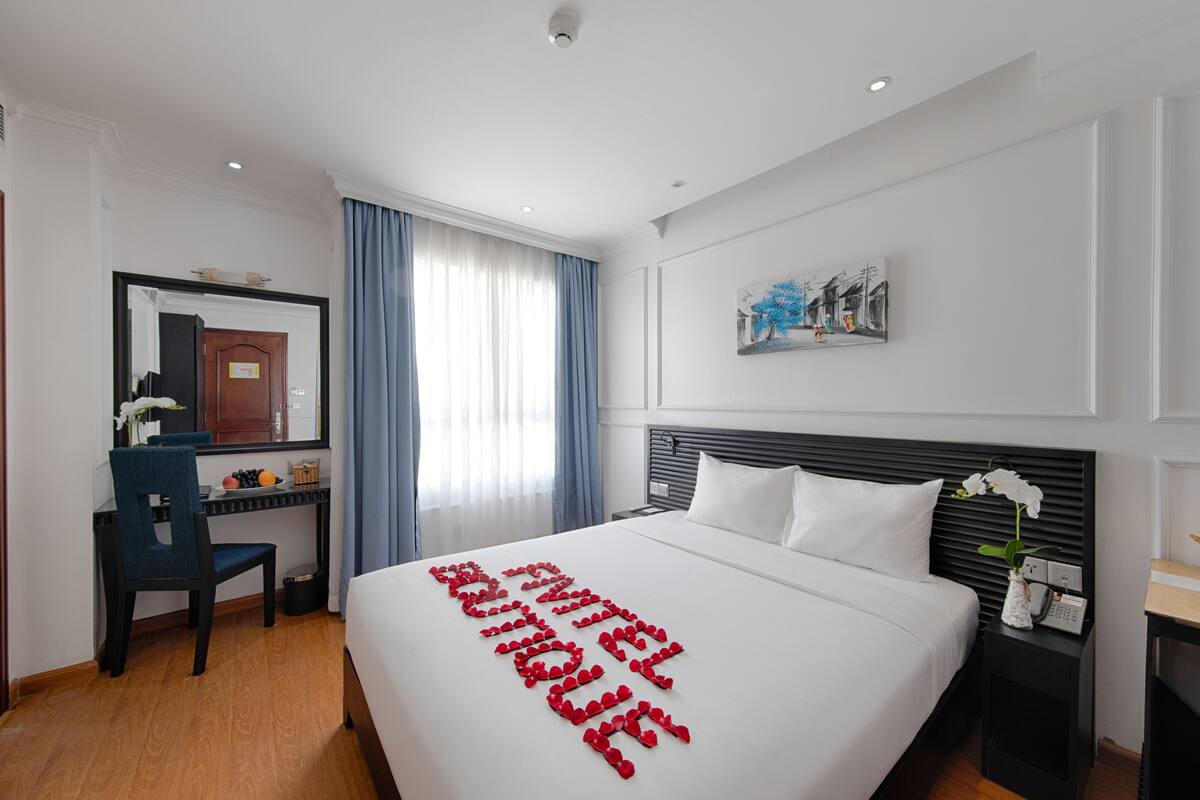 Habitación de hotel con una cama bien hecha, un escritorio con una silla, un teléfono y un cuadro en la pared.