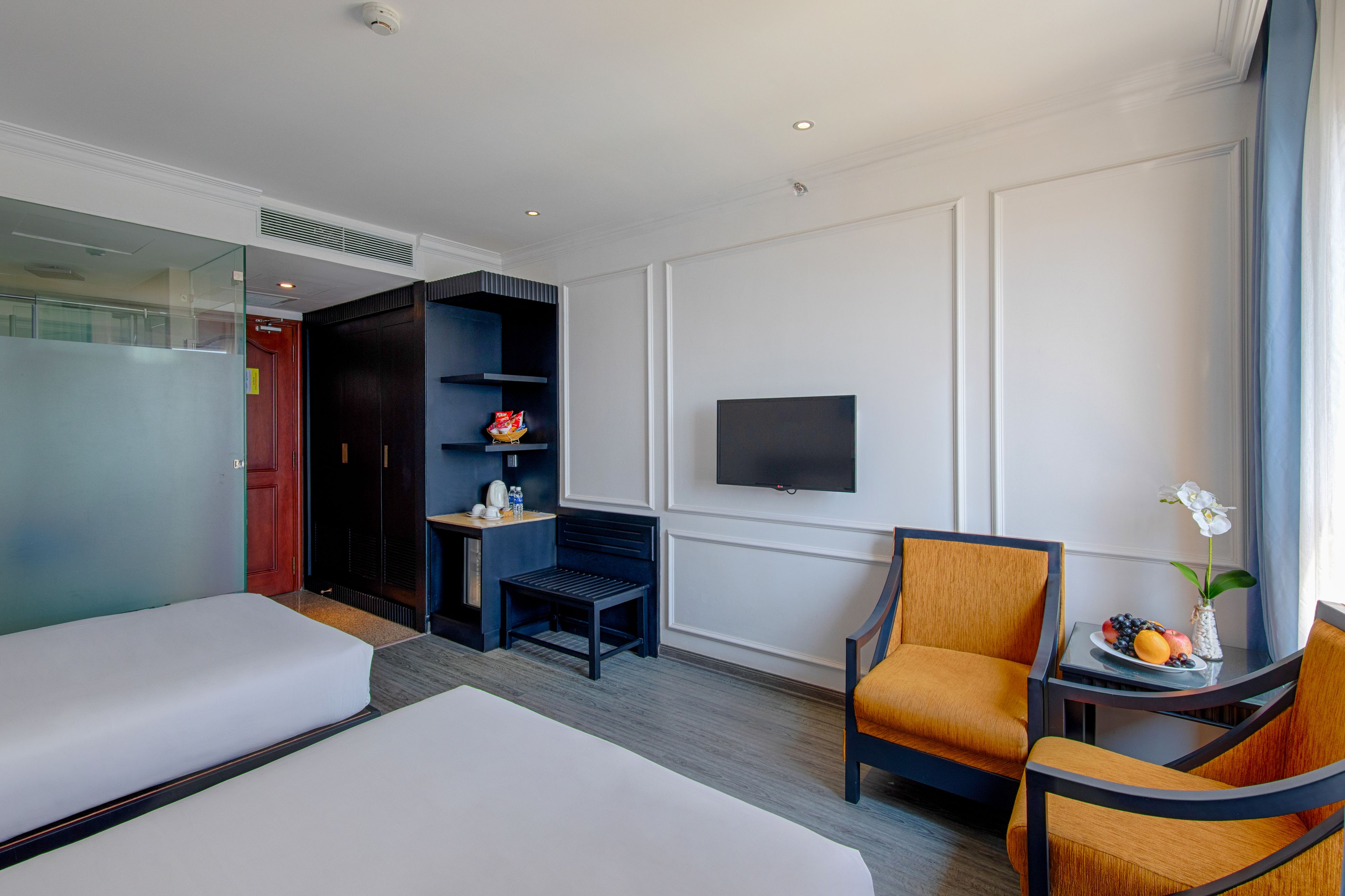 A hotel room with two beds, a TV, a small table with fruit, and a chair.