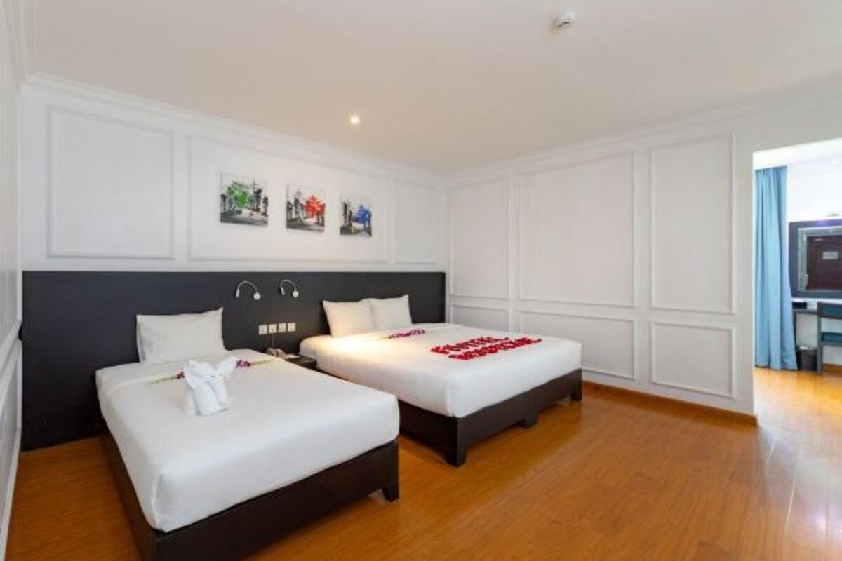 A hotel room with two beds, wooden flooring, white walls, and a dark headboard.