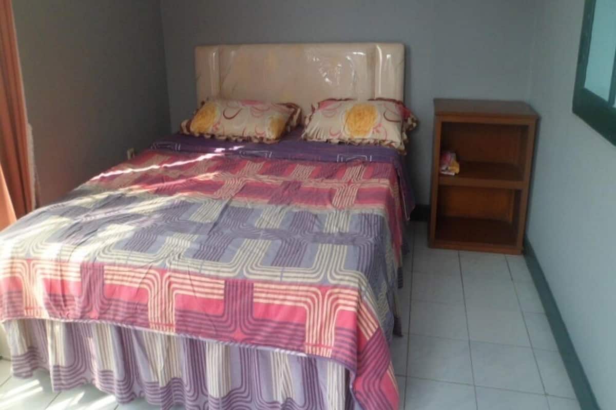 Un dormitorio con cama, almohadas, una mesita de noche y una ventana.