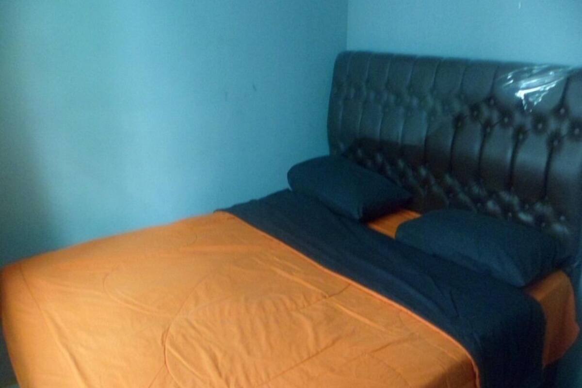 Una cama con una colcha naranja y azul, un cabecero capitonado y un suelo de baldosas.