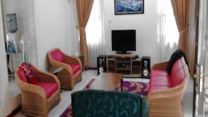 A living room with a television, two wicker chairs, a sofa, and a patterned rug. - Kota Bunga CC (Cipanas)