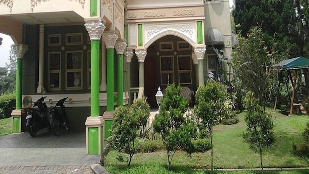 A large, ornate building with a prominent entrance, multiple windows, and green pillars. - Kota Bunga CC (Cipanas)