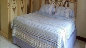 A bed with a striped bedspread, a wooden headboard with intricate carvings, and a wardrobe with ornate designs. - Kota Bunga CC (Cipanas)