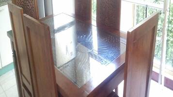 A dining table with a glass top surrounded by wooden chairs with intricate carvings.