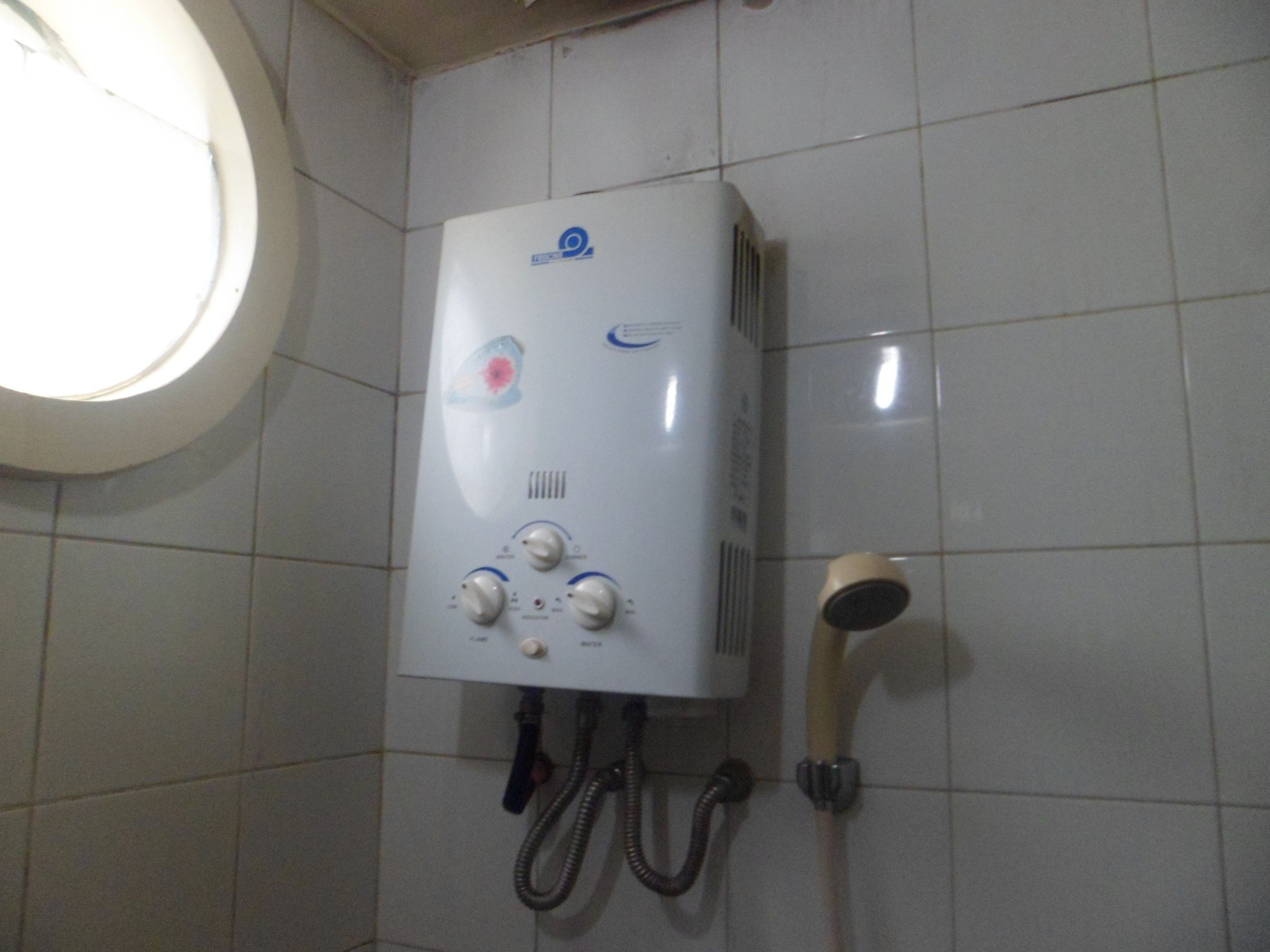A bathroom with a white tiled wall, a white showerhead, and a white water heater with control knobs.