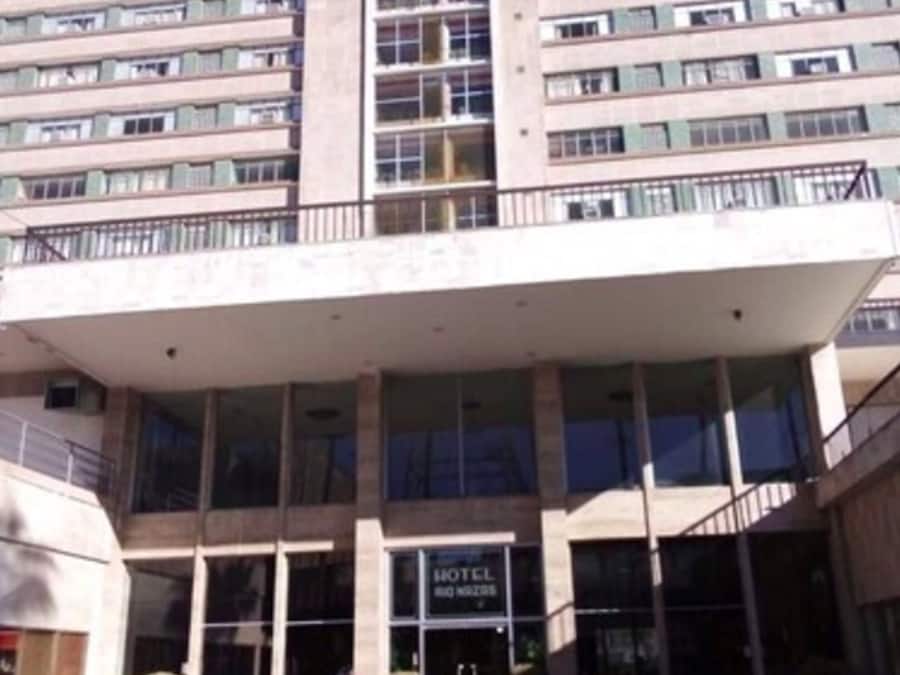 Un hotel de varios pisos con una entrada central, grandes ventanales y un techo plano.