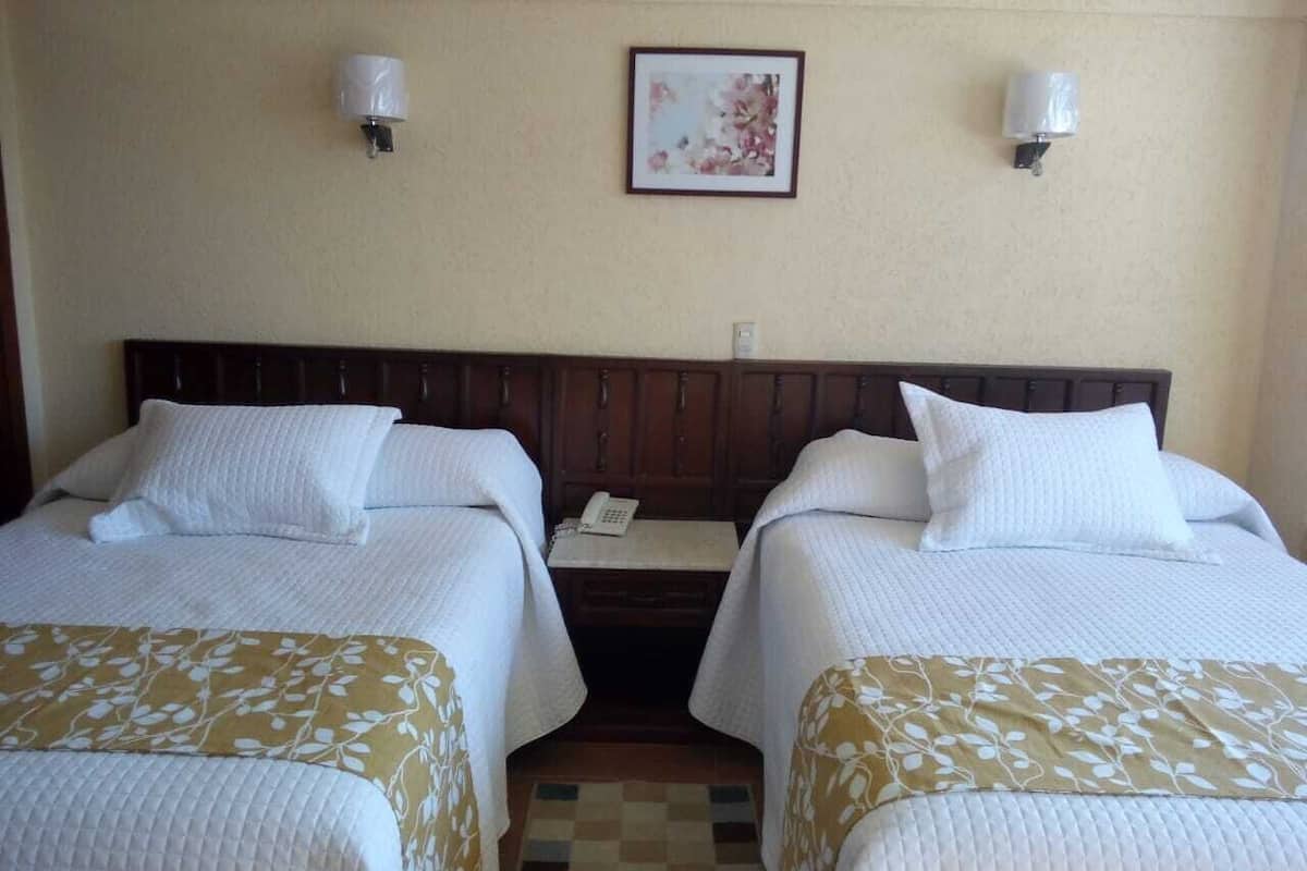 Una habitación de hotel con dos camas, una mesita de noche con un teléfono y un cuadro en la pared.