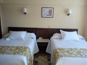 A hotel room with two beds, a small bedside table with a phone, and a framed picture on the wall.