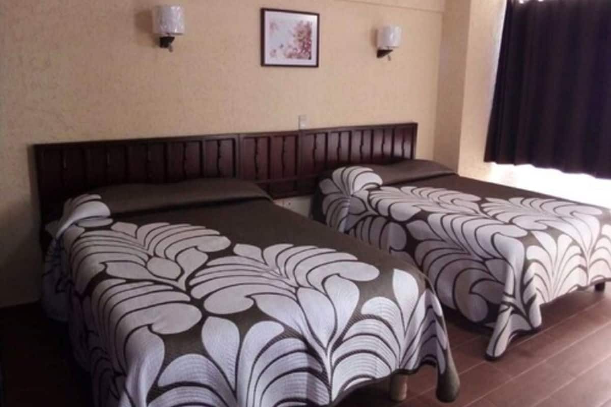 Habitación de hotel con dos camas, cada una con una colcha estampada, cabecero y dos lámparas fijadas a la pared.