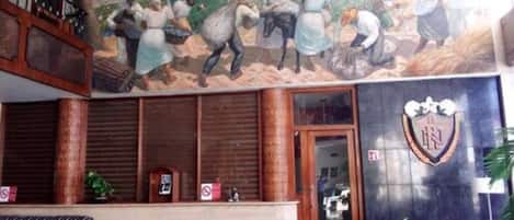 Um hall com um mural retratando uma cena rural, um balcão de recepção e um logotipo na parede.