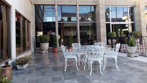 Un patio con piso de mármol, sillas de hierro forjado blanco y plantas en macetas.