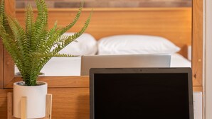 A laptop on a wooden table with a potted fern beside it, a bed with white bedding in the background, and a brick-patterned wall. - All Seasons Motel Armidale (Armidale)