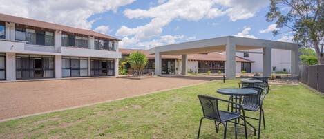 A courtyard with a covered seating area and a building with multiple windows and a tiled roof.