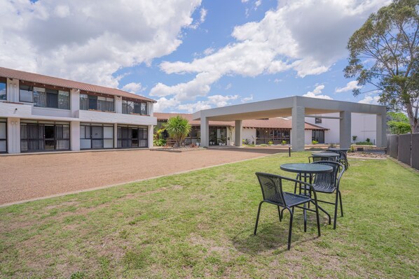 A courtyard with a covered seating area and a building with multiple windows and a tiled roof. - All Seasons Motel Armidale (Armidale)