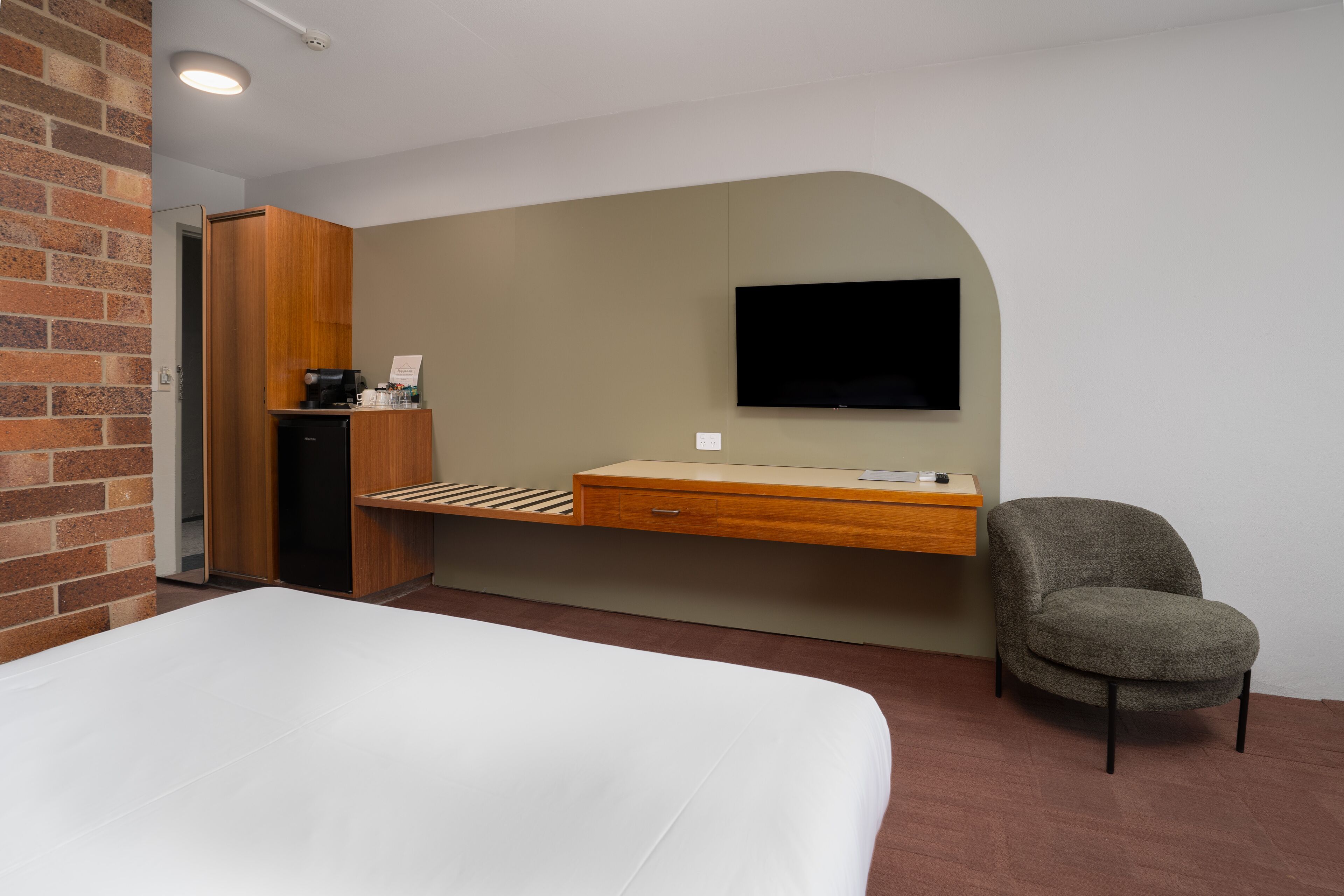 A hotel room with a bed, a desk with a flat-screen TV, a chair, and a coffee machine.