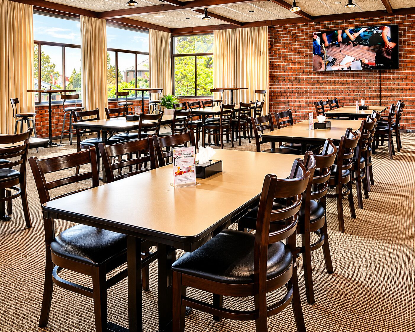 A restaurant with multiple tables and chairs, large windows, and a brick wall.