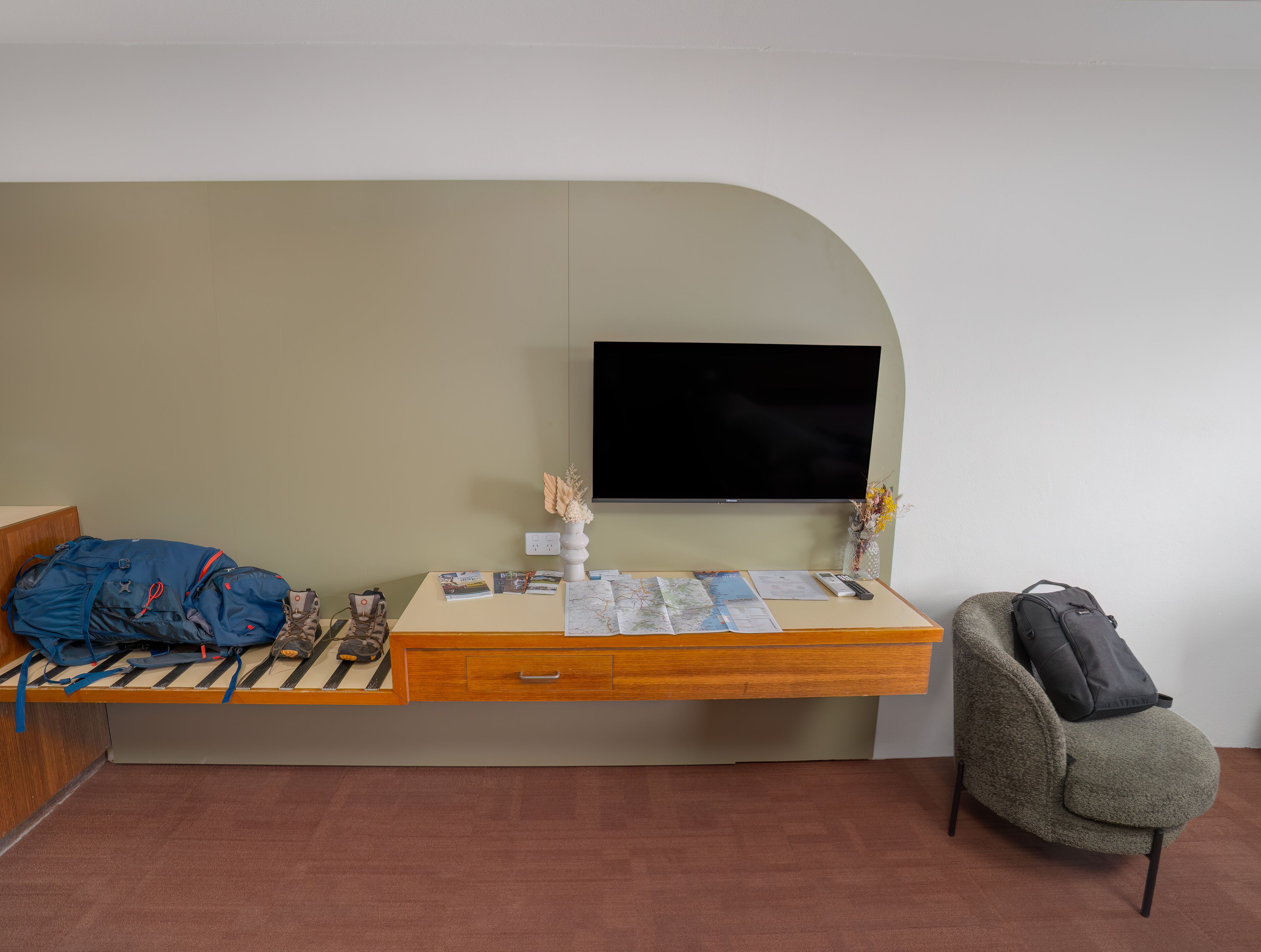 A room with a bed, a desk with a flat-screen TV, a chair, and a backpack.