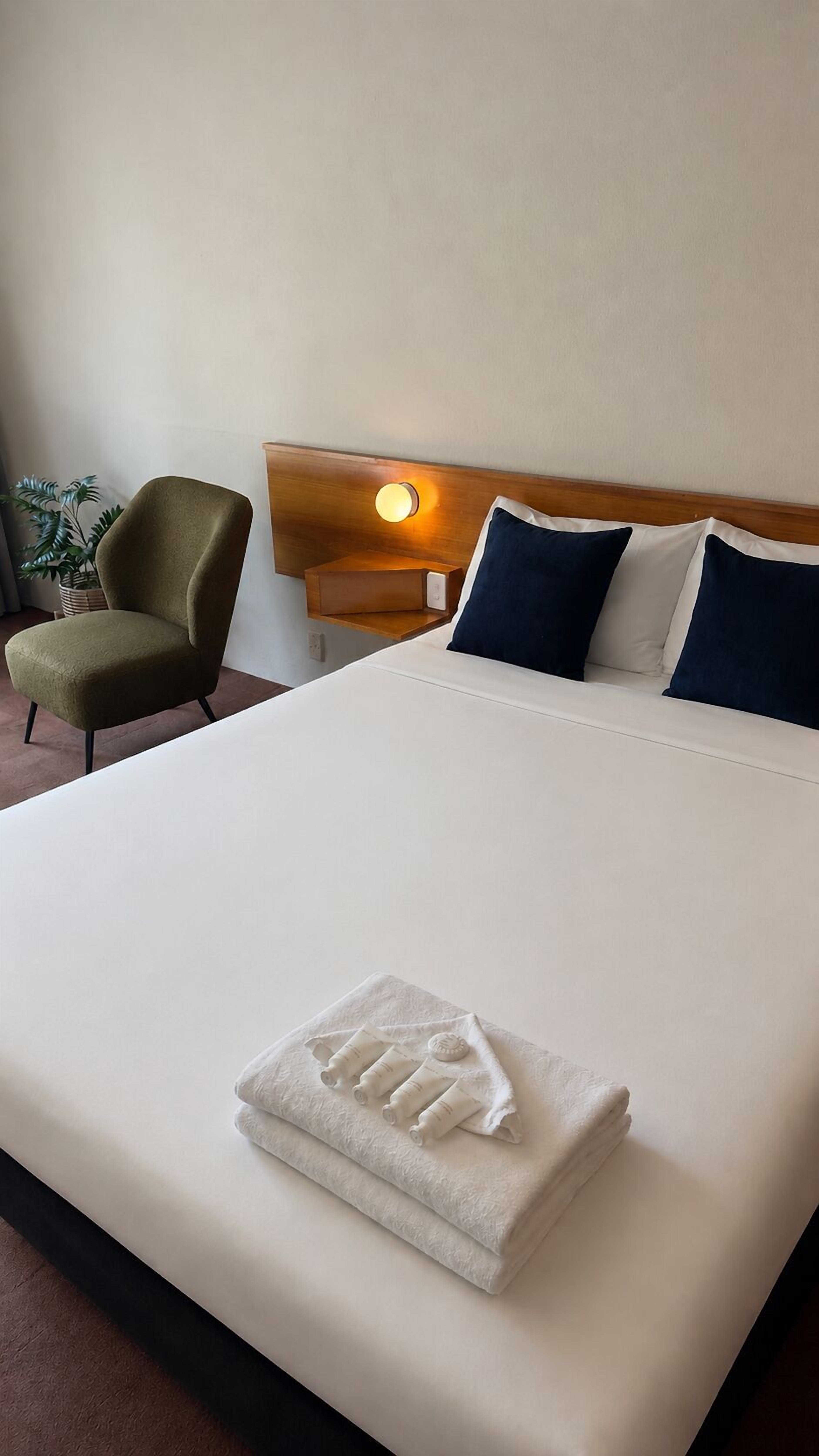 Un lit bien fait, avec une serviette pliée, une tête de lit en bois et une lampe de chevet.