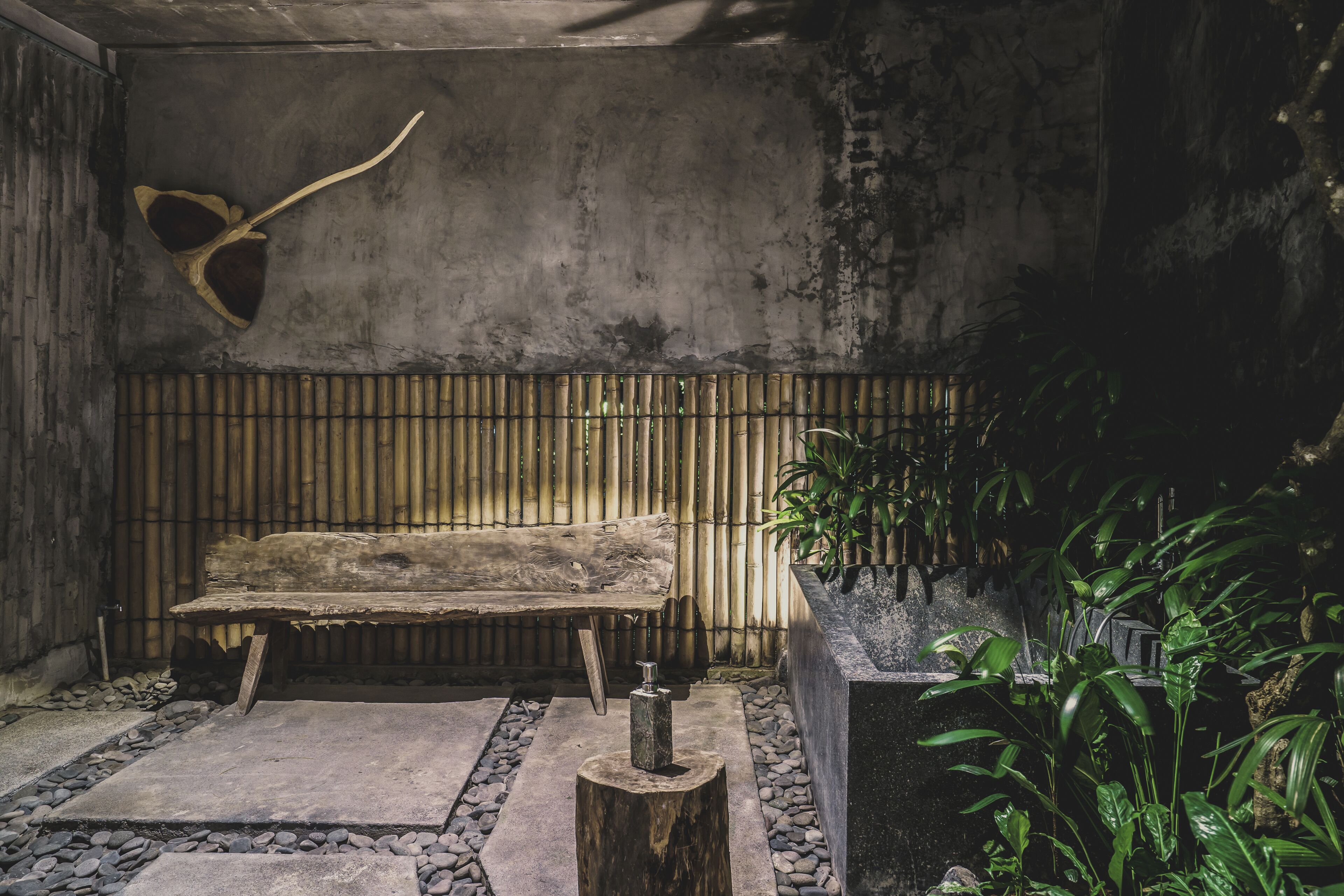 A rustic interior with a wooden bench, a bamboo wall, and a planter with green plants.