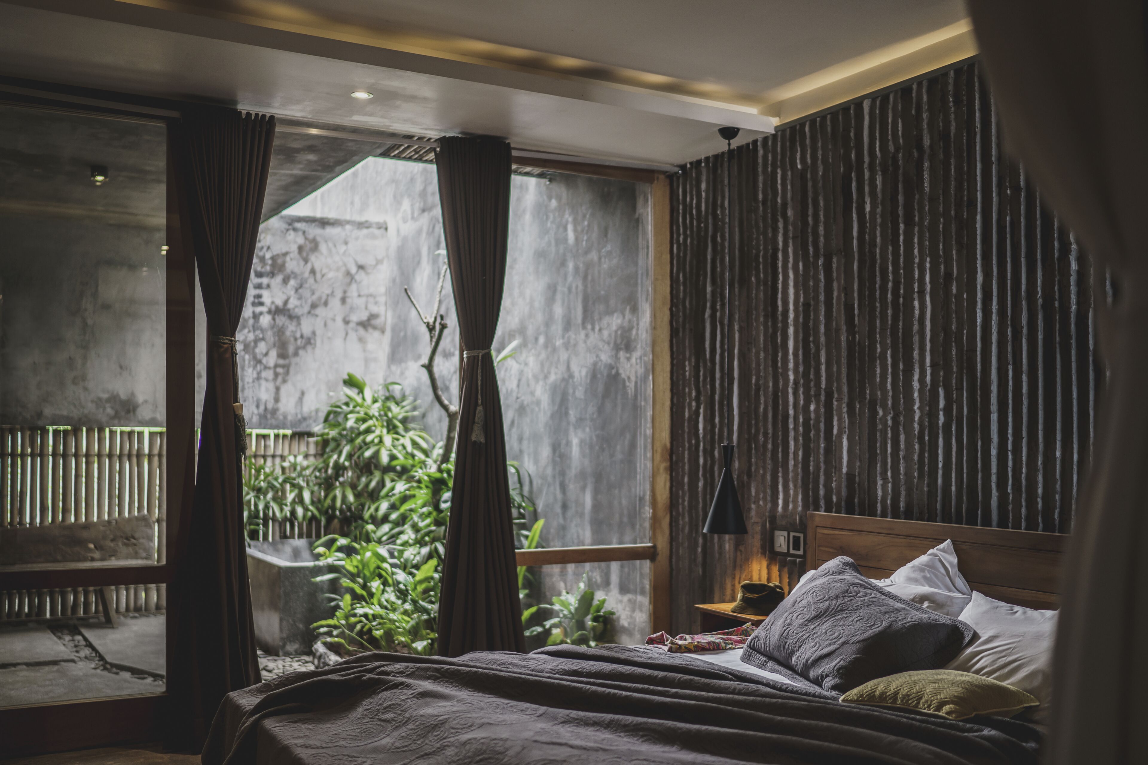 A bedroom with a large bed, wooden headboard, and a view of a garden through a window.