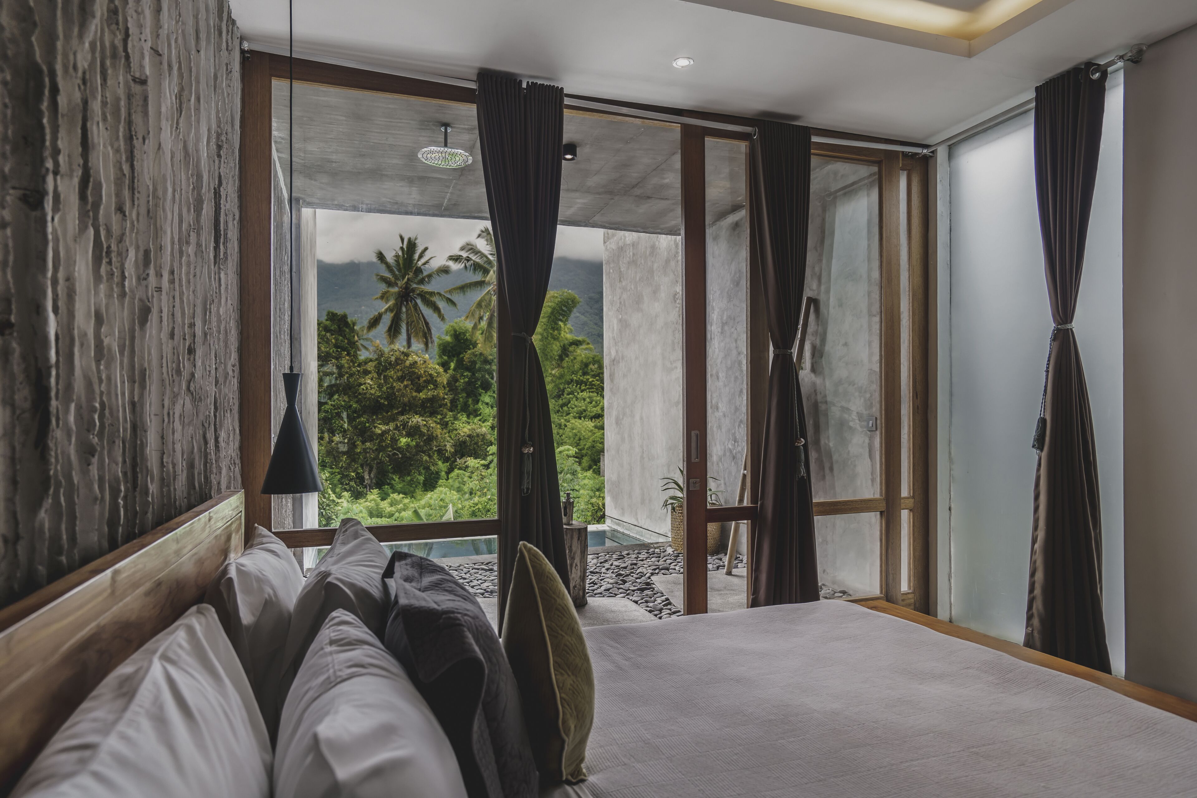 A bedroom with a large bed, wooden headboard, and a view of lush greenery through a sliding glass door.