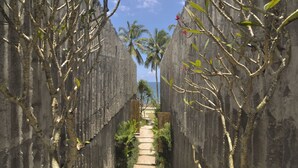 Un sentier bordé de murs de pierre qui mène à une plage où se dressent des palmiers et d’où l’on a une vue dégagée sur l’océan.