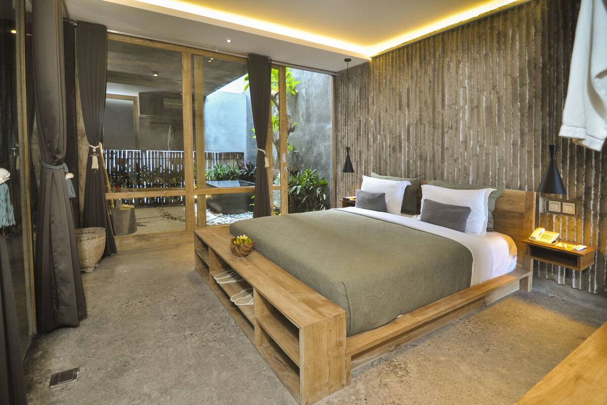 A modern bedroom with a large bed, wooden bench, and a view of a garden.