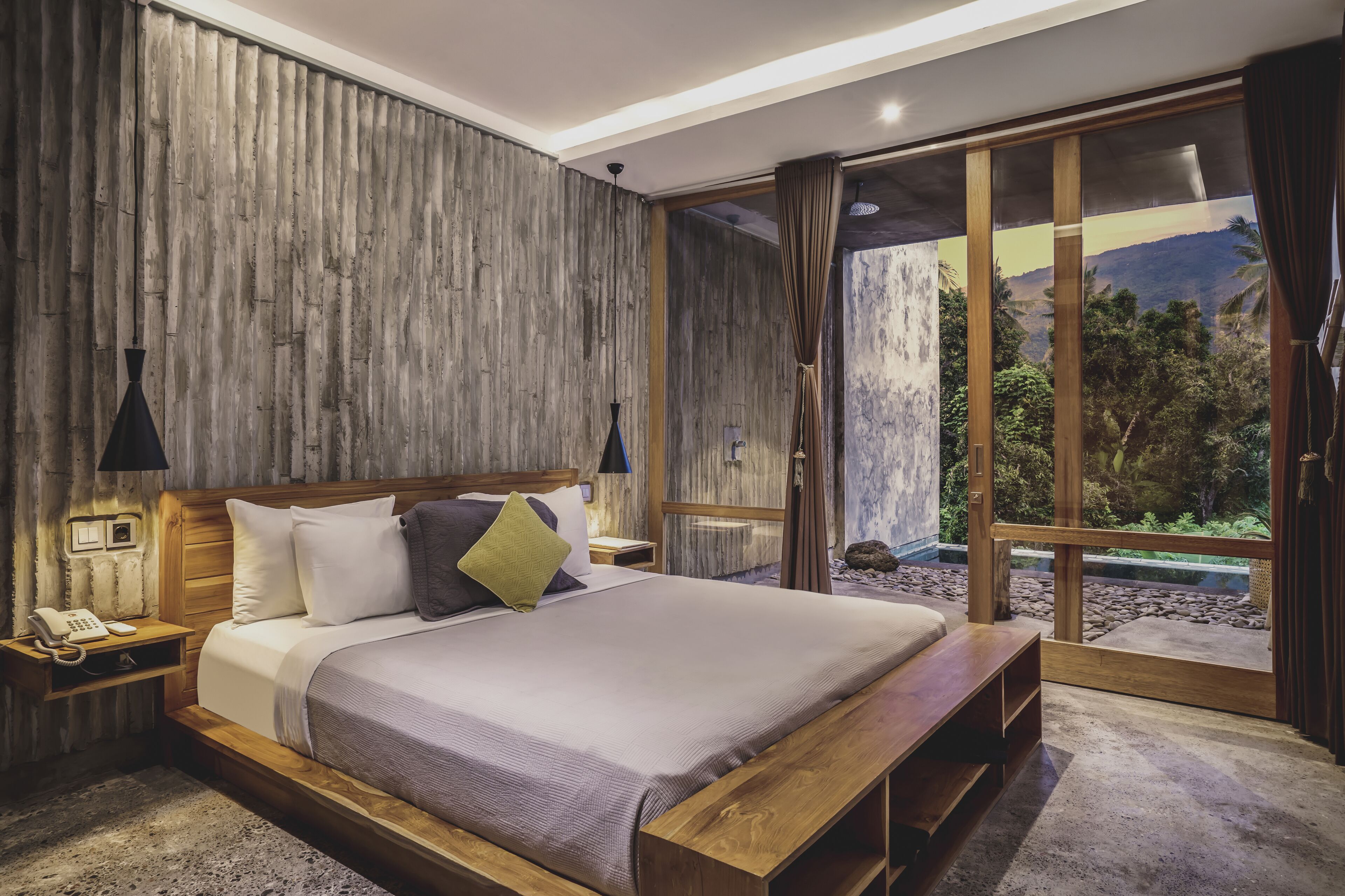 A bedroom with a large bed, wooden headboard, and a view of a mountainous landscape through large sliding glass doors.