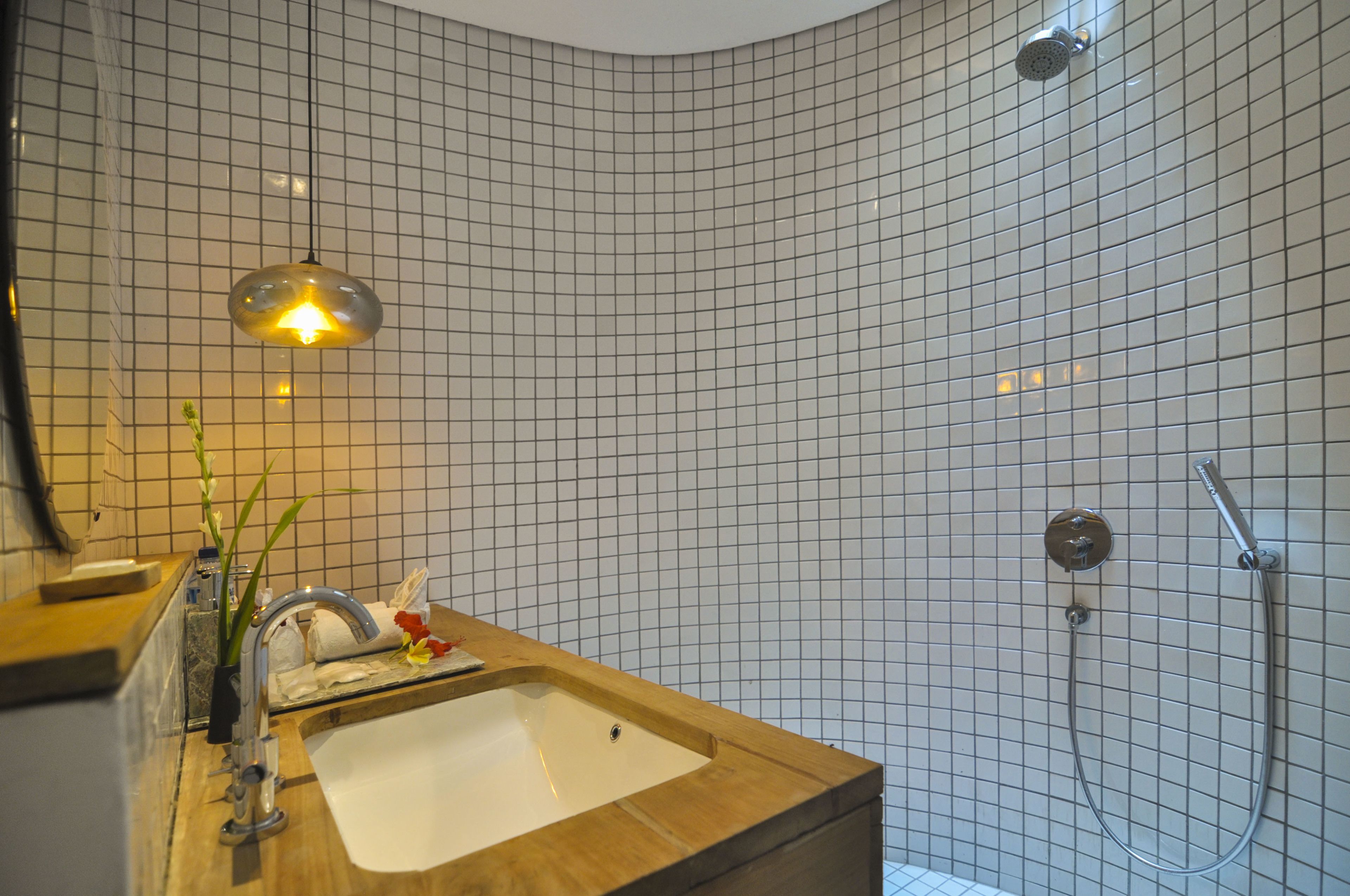 A bathroom with a wooden vanity, a sink, a mirror, a shower with a handheld showerhead, and a grid-patterned tiled wall.