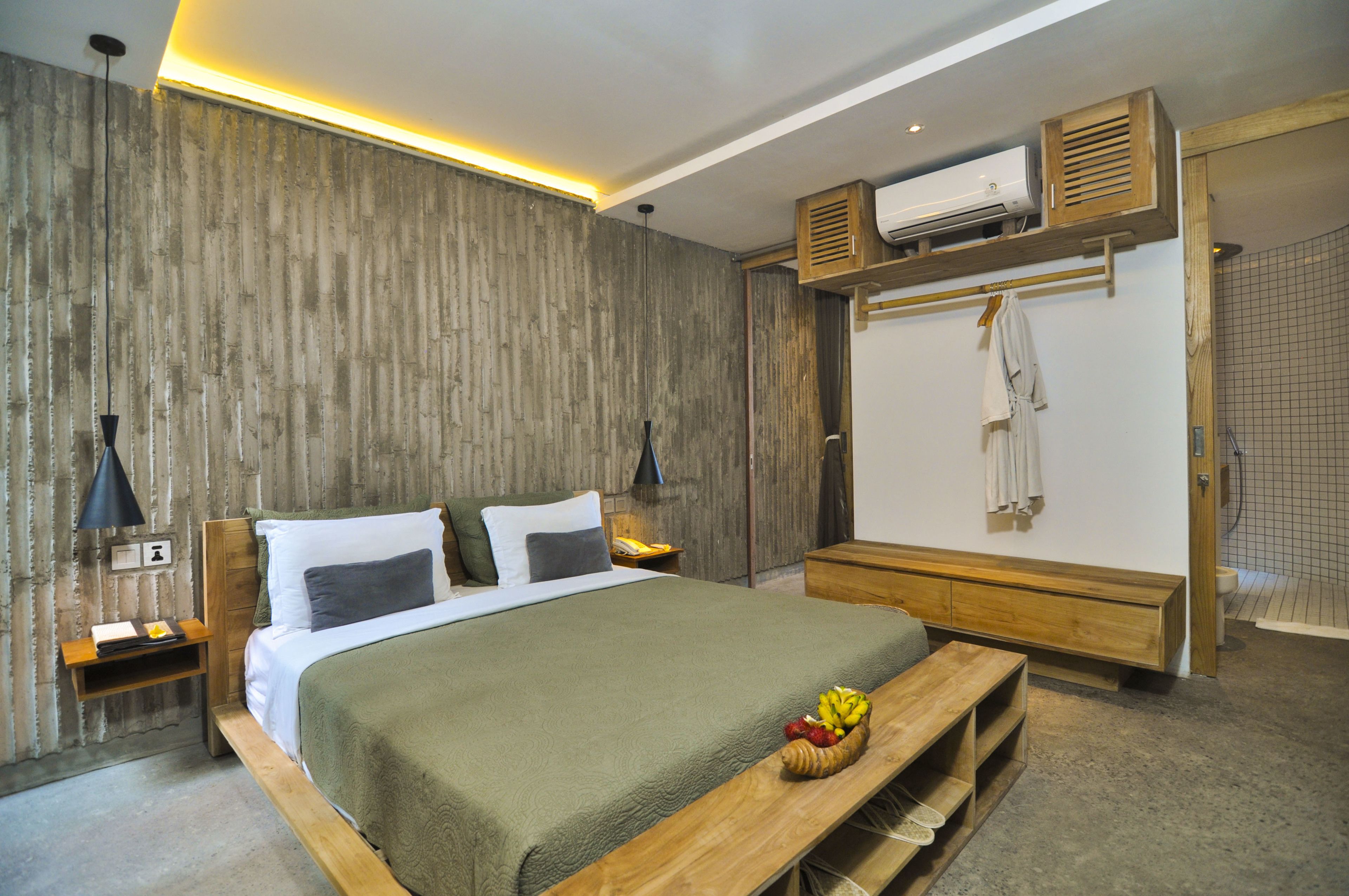 A modern bedroom with a large bed, wooden headboard, bedside tables, a bench with fruit, a wardrobe, and a shower area.