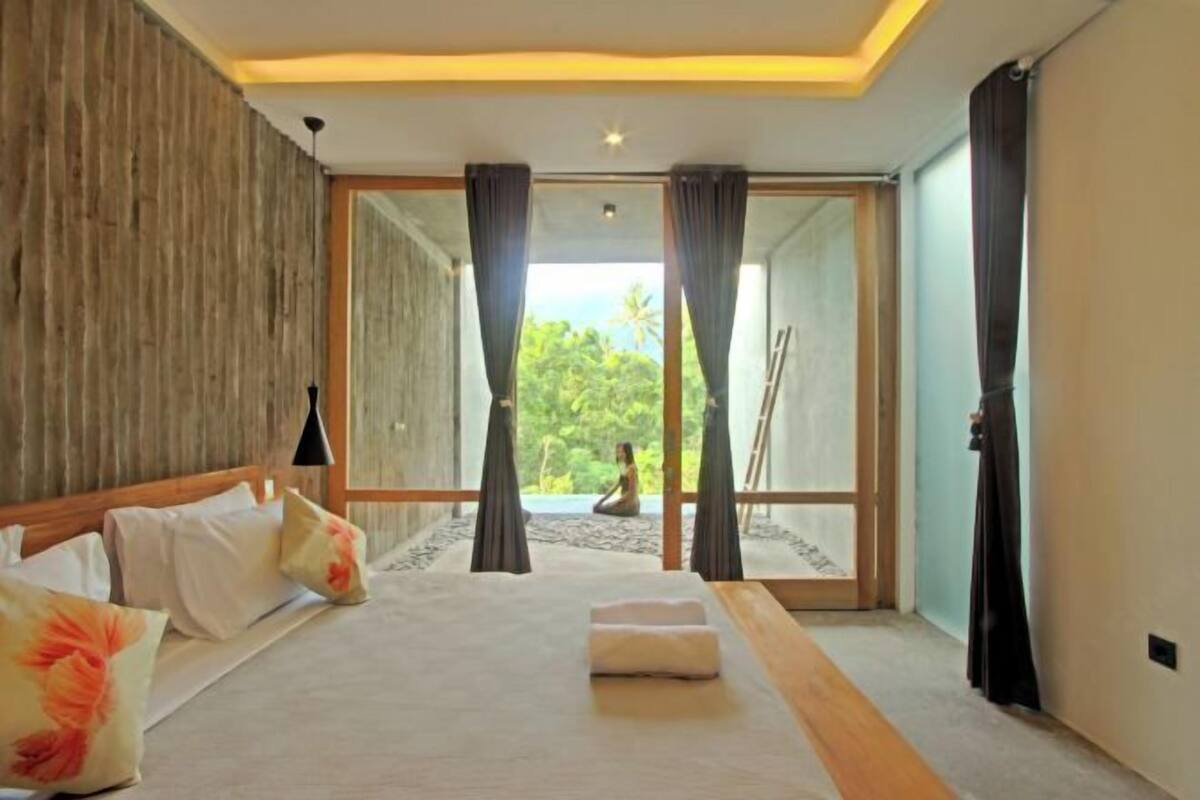 A bedroom with a large bed, a wooden headboard, a view through a glass door, and a ceiling light.