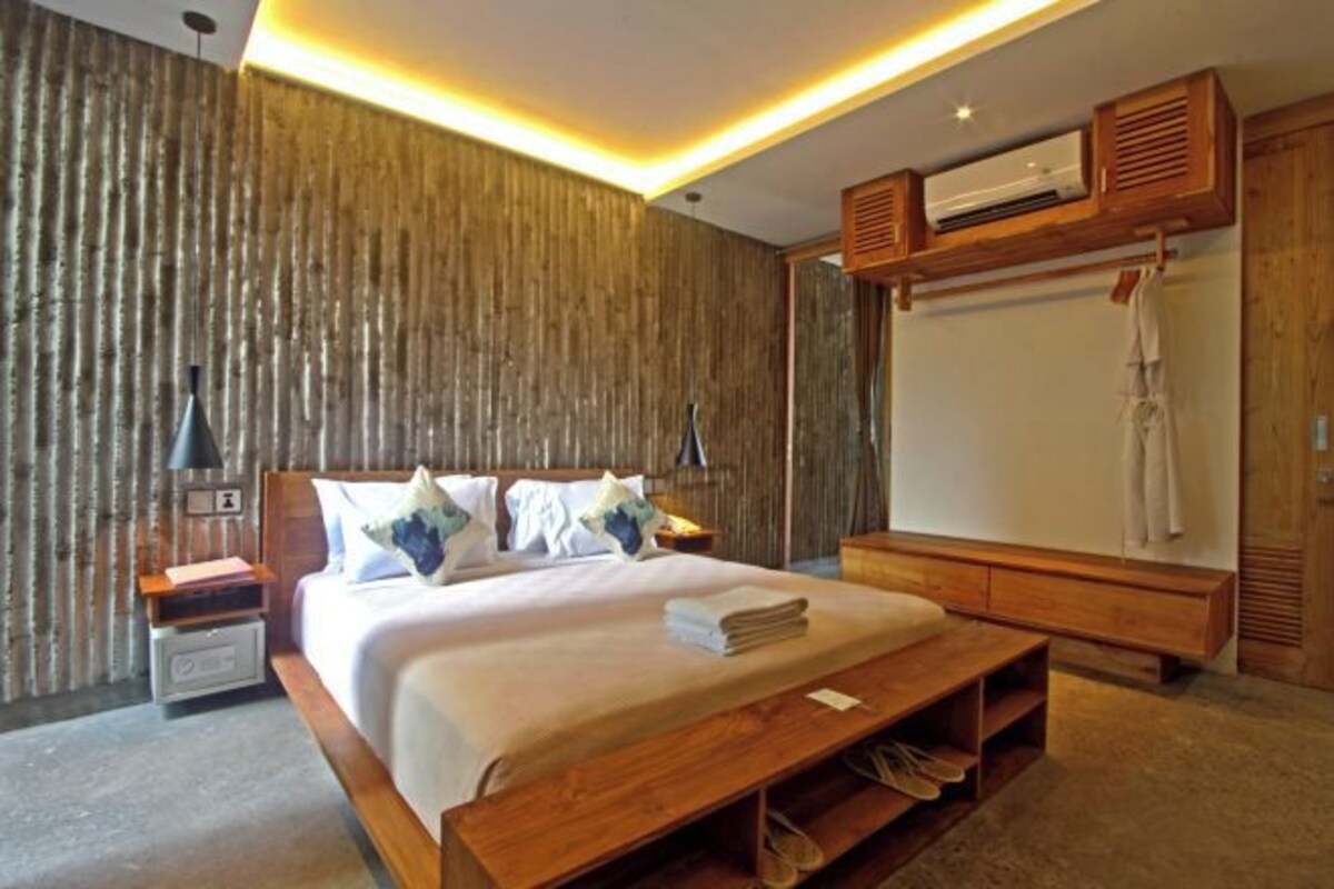 A modern bedroom with a large bed, wooden headboard, bedside tables, a bench, and a wardrobe.