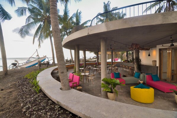 Un café frente a la playa con terraza, palmeras y vistas al mar.