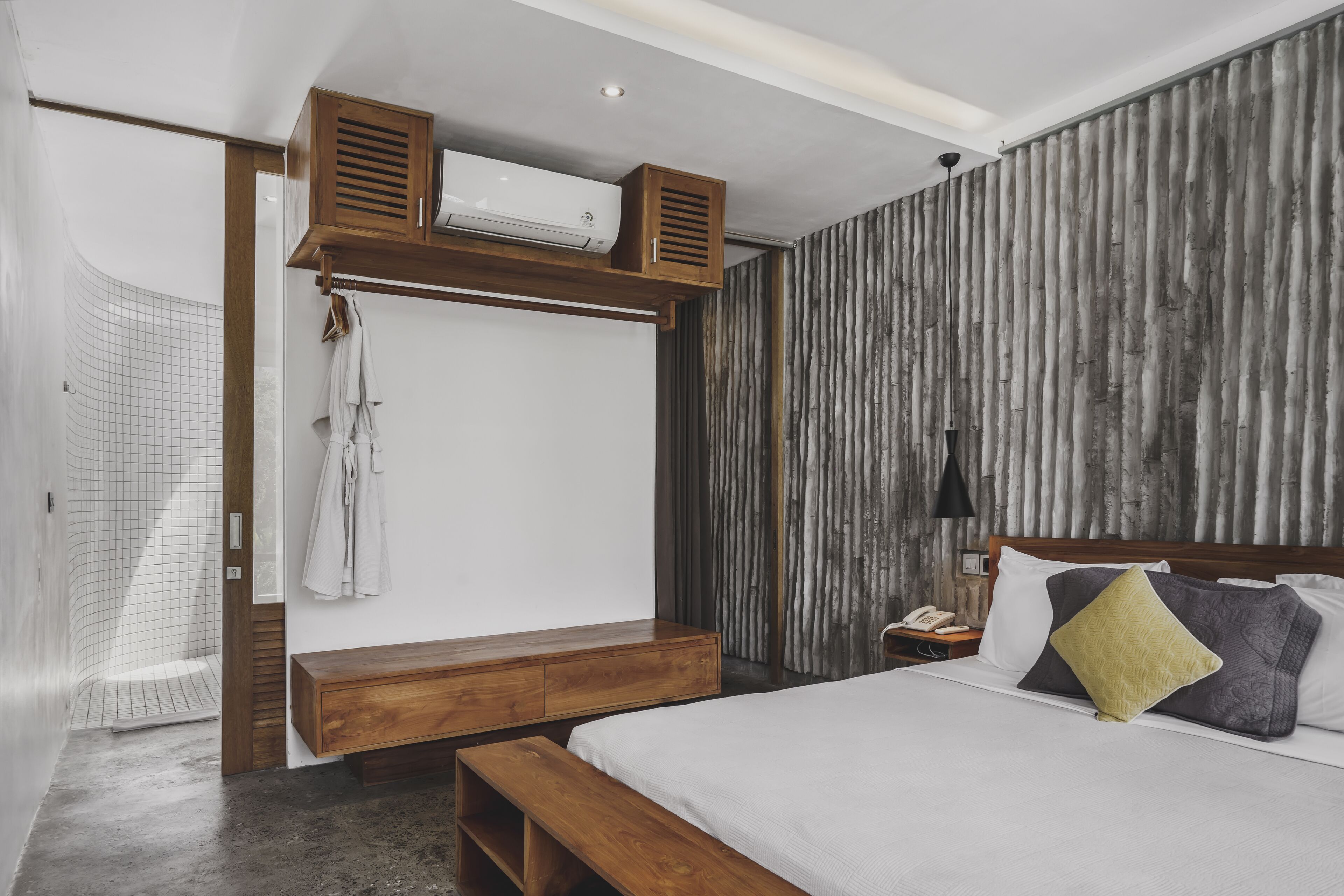 A modern bedroom with a wooden bed frame, a bench, a hanging robe, and a built-in air conditioning unit.