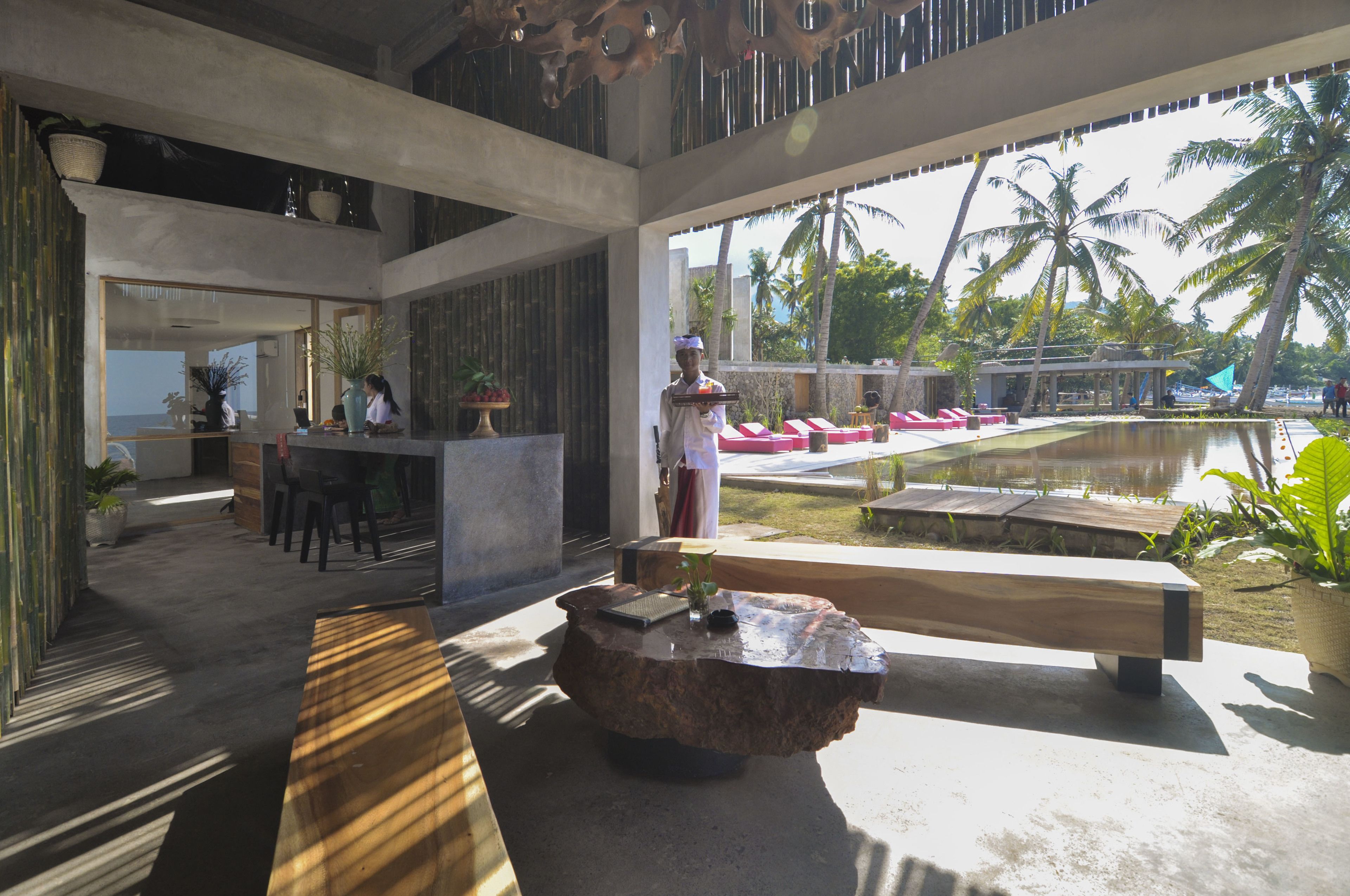 A modern lobby with a reception desk, seating area, and a view of a pool and palm trees.