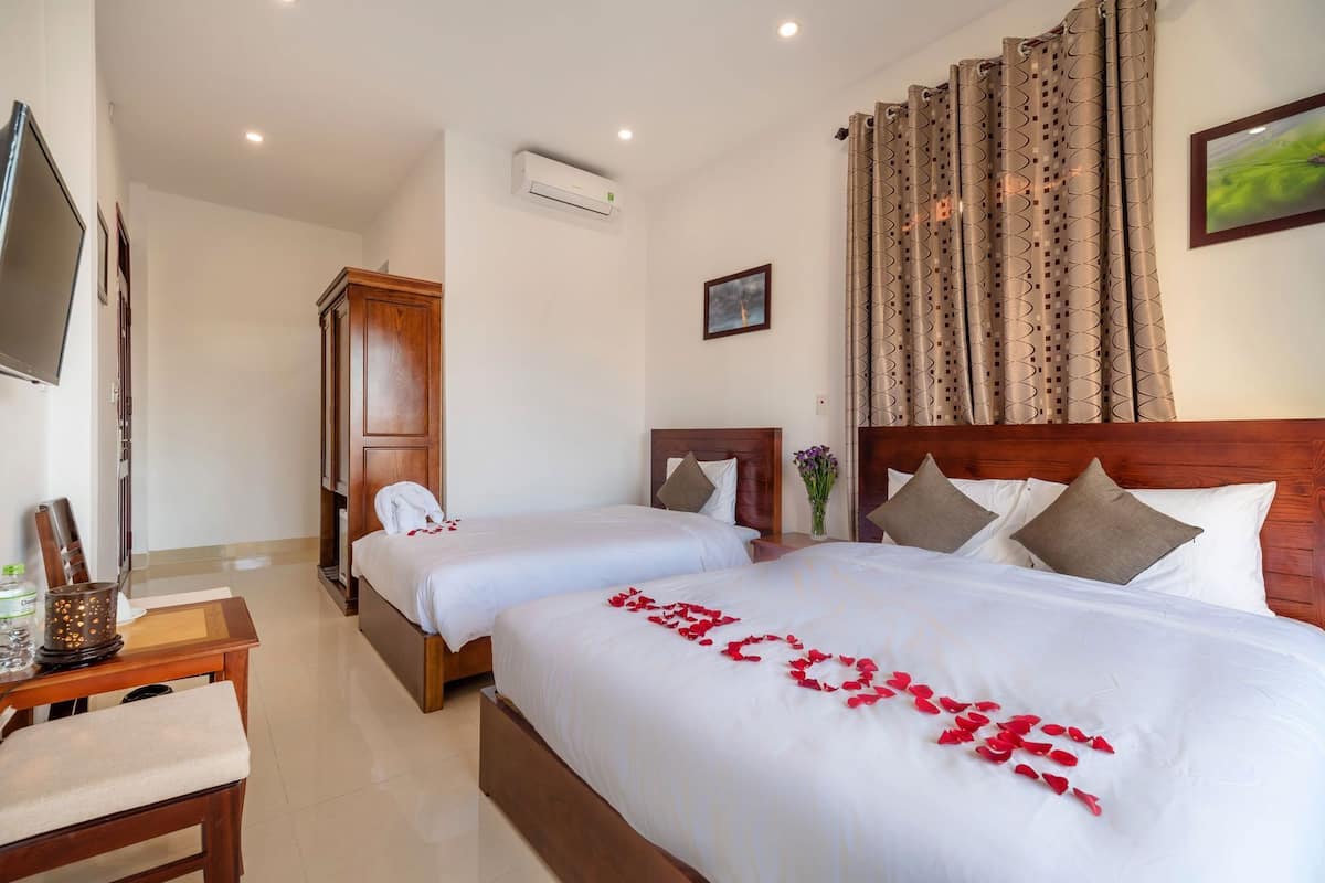 A hotel room with two beds, a TV, a wooden cabinet, and a wall-mounted air conditioner.